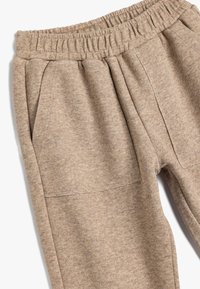 Beige Jogginghose aus weichem Material, mit elastischem Bund, Seitentaschen und einer strukturierten Oberfläche mit einem dezenten Melange-Muster.