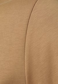 Gros plan sur un tissu beige montrant deux sections avec des textures de tricot distinctes séparées par une couture.