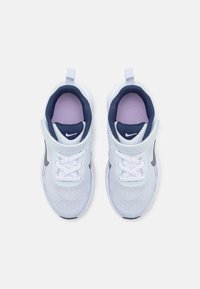 Para białych i fioletowych sneakersów Nike z granatowymi akcentami, z rzepami i sznurowadłami, widziana z góry na białym tle.