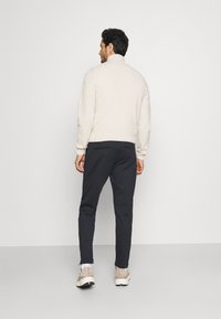 Jersey de punto beige claro con cuello alto y puños acanalados, combinado con pantalones ajustados de color navy oscuro, que cuentan con bolsillos laterales y aberturas en los tobillos.