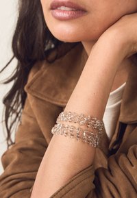 Clear beaded bracelet featuring three strands of irregular-shaped beads, showcasing a light reflective quality. Worn on a light skin tone.