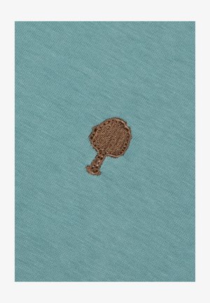 Tissu turquoise avec une finition texturée, présentant un petit motif d'arbre brodé en marron, centré sur le tissu.