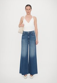 Wide-leg blue jeans made of denim, paired with a white sleeveless top and a textured beige handbag. Footwear features a pointed toe design.