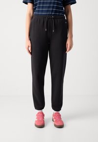 Sorte treningsbukser med snor i livet, mansjetter ved anklene og en jevn tekstur, kombinert med rosa sneakers med hvite detaljer.