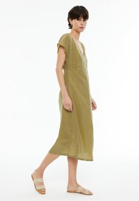 Olivengrünes Kleid mit kurzen Ärmeln, tiefem V-Ausschnitt und lockerer Passform, aus einem weichen, leichten Stoff gefertigt.