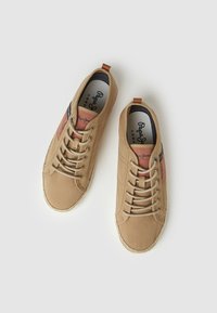 Zapatos casuales color beige con un upper texturizado, acentos en coral contrastantes, puntera redonda y un detalle decorativo de costura a lo largo de la suela.