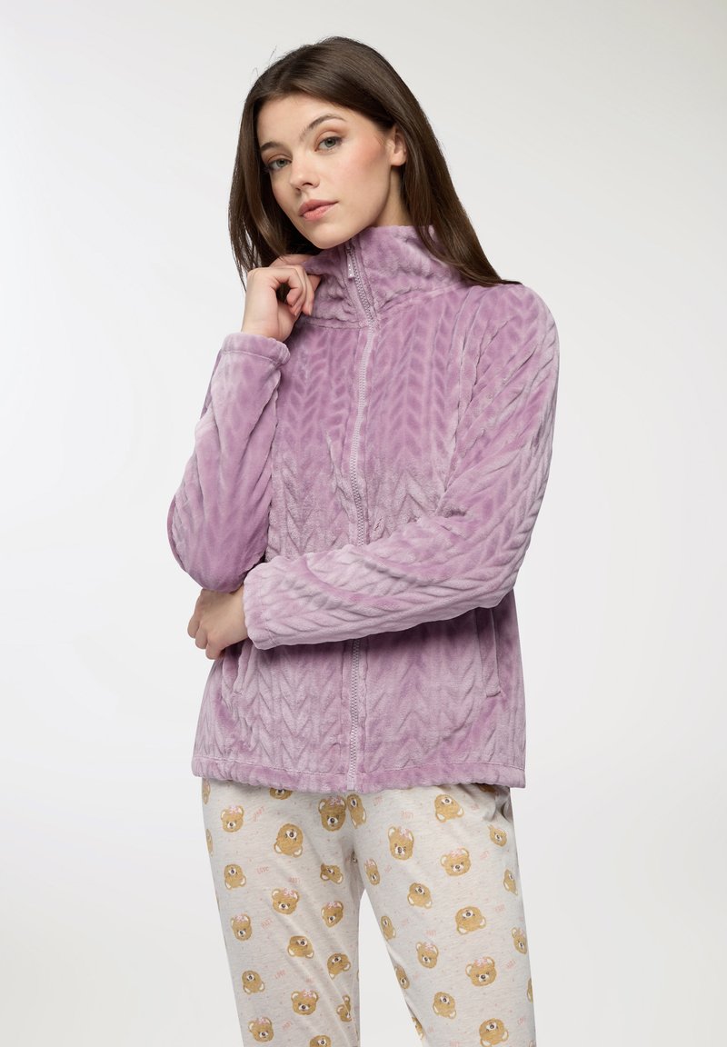 Giacca in pile viola con colletto alto, motivo a zig-zag testurizzato, chiusura con zip e maniche lunghe, abbinata a pantaloni da pigiama chiari con stampe di orsetti.