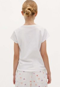 White cotton t-shirt with short sleeves, round neck. Worn with light-colored shorts featuring multicolored flower embroidery on pockets.