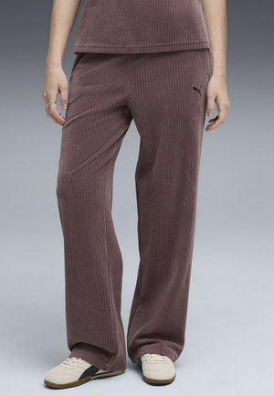 Pantaloni di velluto a coste di colore mauve, caratterizzati da strisce verticali, una vestibilità rilassata e un piccolo logo vicino ai fianchi. Indossati con sneaker di colore chiaro.