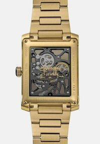 Złocony zegarek ze stali nierdzewnej z prostokątną kopertą, przezroczystą tarczą odsłaniającą skomplikowane mechanizmy wewnętrzne oraz bransoletą w formie ogniw.