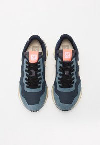 Scarpe da ginnastica navy e azzurro chiaro con lacci neri, suola beige e patch logo rosa sulla linguetta. Parte superiore testurizzata con pannelli a contrasto.