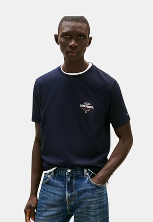 T-shirt in cotone blu navy con scollatura rotonda e dettagli bianchi. Presenta un piccolo logo sul petto ed è abbinato a jeans in denim blu sbiadito.