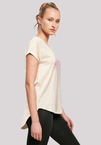 Light beige short-sleeve T-shirt with a V-neck and a slightly longer back hem, featuring colorful text on the front and soft texture.
