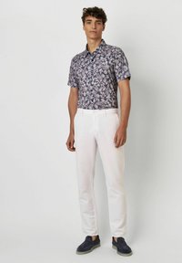 Kurzärmeliges, florales Hemd in Marineblau mit weißen Blattmustern, kombiniert mit weißen Slim-Fit-Hosen und navyfarbenen Slippern.