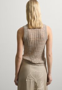 Top sin mangas de punto acanalado beige con un diseño texturizado, combinado con una falda crema que presenta acentos de hojas bordadas en la parte posterior.