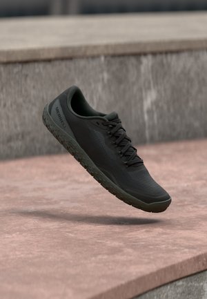 Melnas Merrell sporta kurpes ar teksturētu zoli un šņorēm, kas peld virs rozā toņu akmens virsmas ar betona kāpnēm fonā.