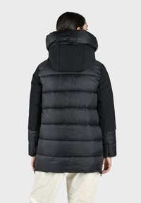 Sort pufferjakke med høj krave, der har et quiltet design, kontrastfarvede ærmer, lynlås-lommer og en glat tekstur.