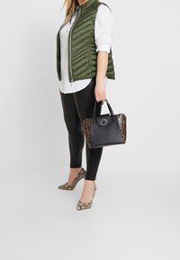 Svart och ormskinsmönstrad handväska med texturmaterial. Grön quiltad väst, vit skjorta och svarta leggings. Ormskinsmönstrade klackar fulländar outfiten.