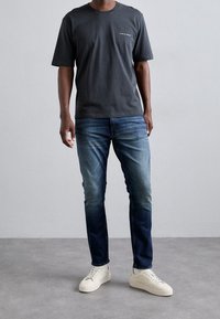 Grå bomullst-shirt med kort ärm, parat med blå denimjeans som övergår från ljus till mörk, och vita sneakers med strukturerade sulor.
