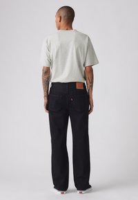 Jeans negri din denim cu un croi drept, având o etichetă din piele bej pe spate, asortați cu un tricou gri cu mânecă scurtă.