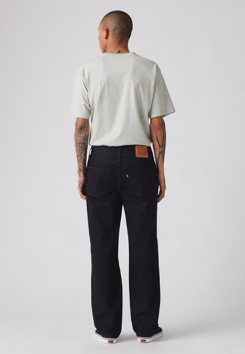 Jean en denim noir à coupe droite, avec une étiquette en cuir beige à l'arrière, associés à un t-shirt gris à manches courtes.