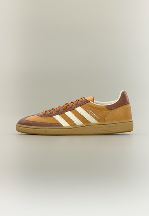 Sneaker Adidas Spezial marrone e tan con strisce bianche, suola in gomma e lacci arancioni mostrato di profilo su sfondo neutro.