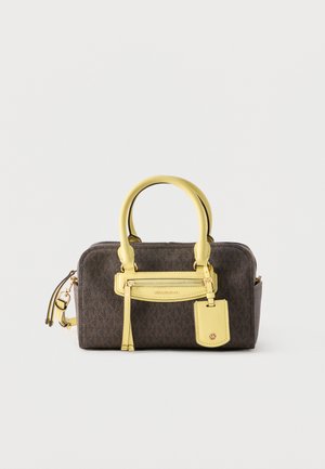 Sac à main texturé marron avec poignées jaunes, poche zippée à l'avant et étiquette suspendue sur un fond blanc uni.