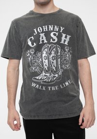 Graphic t-shirt in dark gray with a faded look. Features white print of cowboy boots and text "JOHNNY CASH WALK THE LINE." Short sleeves.