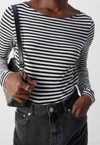 Langarmoberteil mit schwarz-weißen horizontalen Streifen, kombiniert mit dunklen, hoch geschnittenen Jeans und einer schwarzen strukturierten Handtasche.