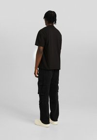 Czarna bawełniana koszulka z krótkim rękawem, zestawiona z czarnymi spodniami typu cargo z wieloma kieszeniami. Model nosi białe trampki.