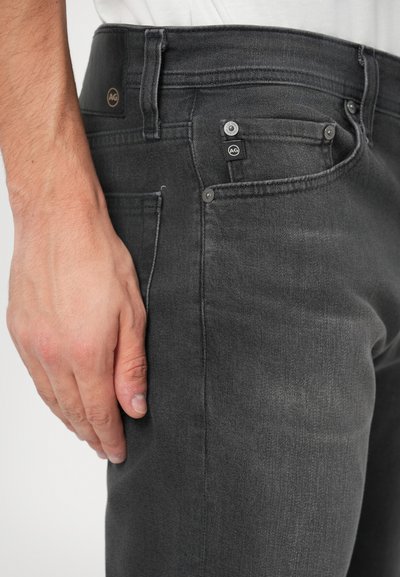 Jeans de ganga cinza com um design ajustado, apresentando um bolso visível, ferragens de metal e uma textura subtil. O tecido parece suave e durável.