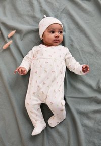 Weißer Babyschlafanzug mit rosa floralem Muster, langen Ärmeln und Füßchen. Aus Baumwollstoff. Passende weiße Mütze mit kleinem Knotendetail.