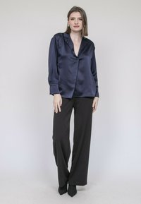 Blouse en satin marine avec un col à revers, des manches longues et une coupe ample, associée à un pantalon noir large taille haute et des talons noirs.