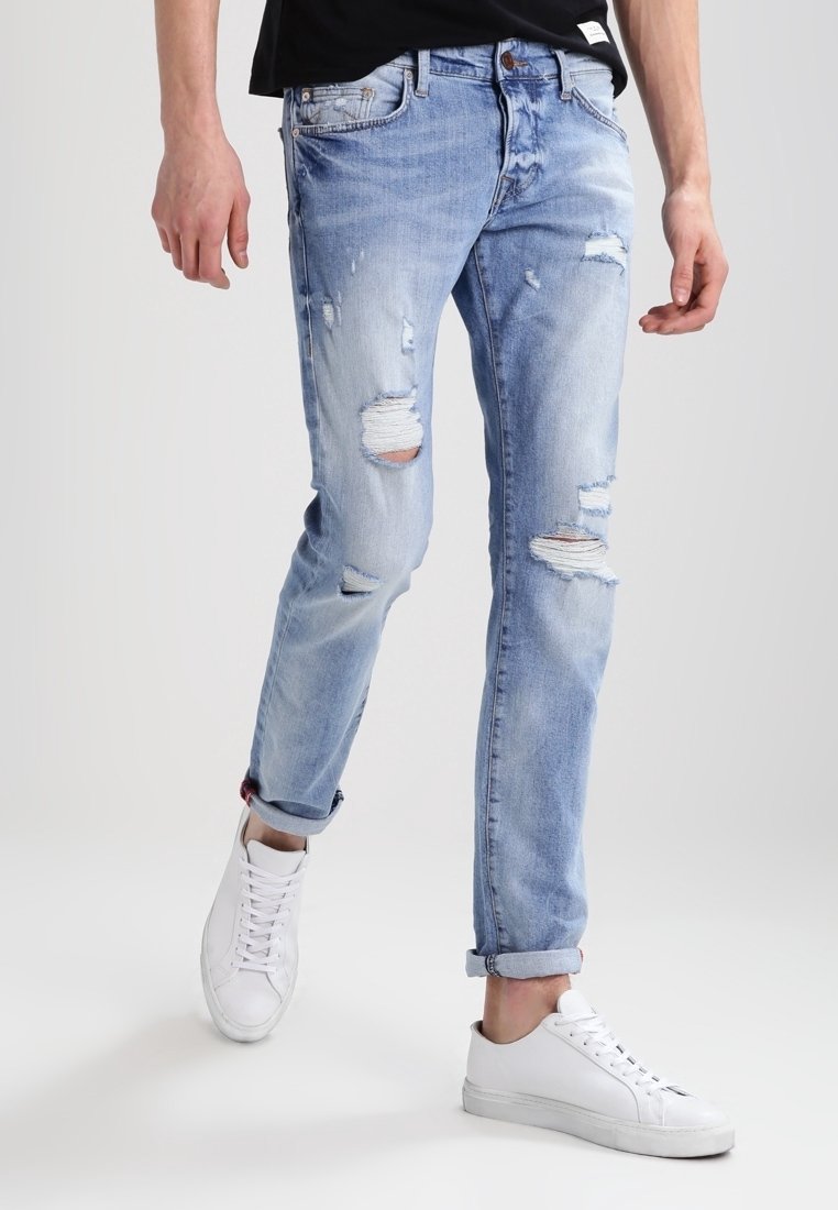 Jasnoniebieskie dżinsy z przetarciami, z podwiniętymi nogawkami i prostym krojem, w połączeniu z białymi trampkami.