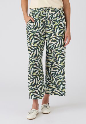 Pantalones de pierna ancha con estampado de hojas verdes, blancas y rosas, cintura elástica con cordón, combinados con zapatos blancos sin cordones.