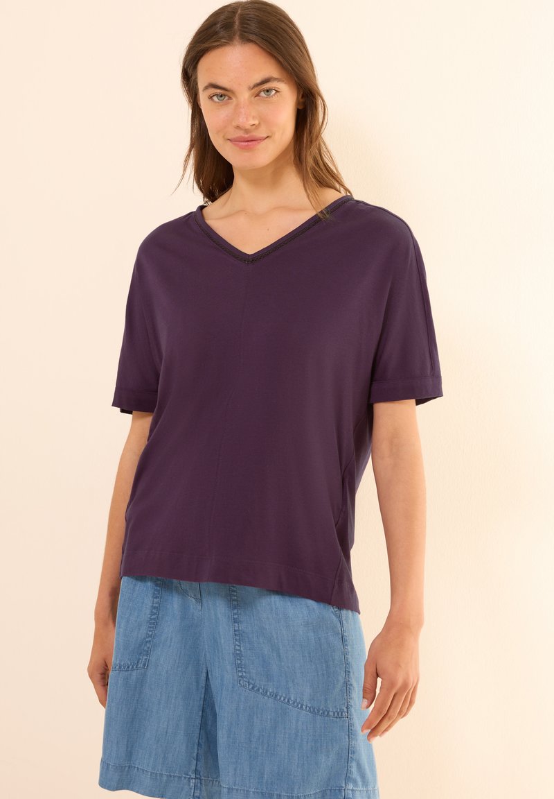 Blusa morada de cuello en V con mangas cortas, hecha de una tela suave. Presenta un corte relajado y una costura sutil a lo largo del escote.