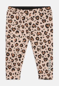 Beige legice s črnim in rjavim vzorcem srčkov in leoparda, besedilo logotipa "Guess" po celotnem oblačilu in vertikalno na spodnjem delu noge.