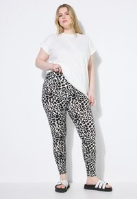 Witte kortekorte mouwen t-shirt gecombineerd met zwart-witte luipaardprint leggings. De model draagt zwarte sandalen met witte accenten.