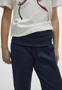 Vit kortärmad t-shirt med ett leopardmönster och ribbade marinblå byxor. Byxorna har en bred, texturerad midja.