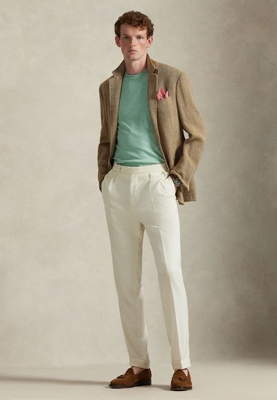 Světlý hnědý blazer se vzorem rybí kosti, mátově zelená košile, krémové kalhoty a hnědé mokasíny s třásněmi. Růžová kapesníček přidává detail.