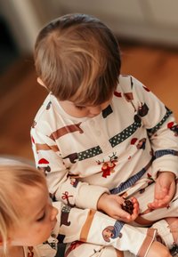 Kerman pyjamat pestyis eläinteemalla, jossa on hirviä, koiria ja lahjoja. Napit kauluksessa ja siniset yksityiskohdat.