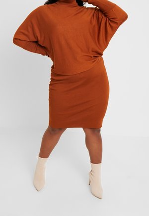 Personne portant une robe-pull col roulé orange rouille avec de longues manches chauve-souris et des bottines beiges à talons aiguilles pointues.