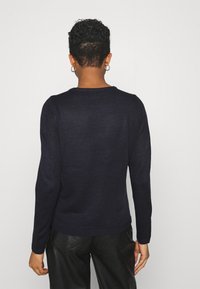 Pull en maille navy avec manches longues, col rond et poignets en côtes, associé à un pantalon en cuir noir. La texture semble douce et lisse.