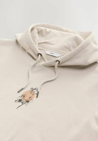 Sudadera beige con cordones y gráfico floral con un acento naranja. Textura suave, corte regular, con abertura para bolsillo tipo canguro.