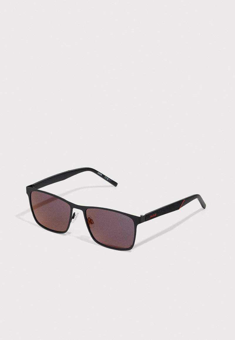 Rechteckige Sonnenbrille mit schwarzem Metallrahmen, braunen Verlaufslinsen und strukturierten schwarzen Bügeln mit einem roten Streifen und Logodetails.