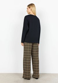 Svart långärmad topp med avslappnad passform, kombinerad med högmidjade rutiga vida byxor i svart och beige, med texturerad tyg.