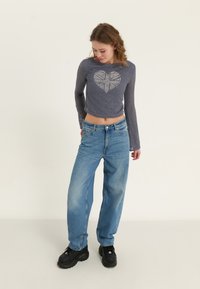 Marineblå mesh langermet topp med hjerte-design, kombinert med lys blå vide jeans og svarte klumpete sko. Glatt og avslappet passform.