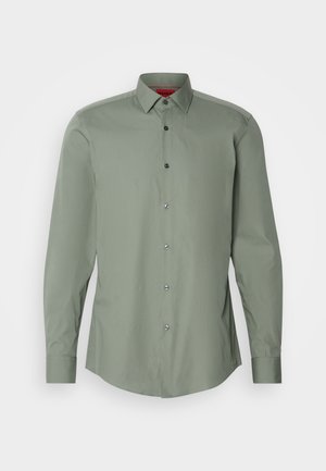 Ilgi piedurkņu krekls bālā zaļā krāsā, viegls audums. Aprīkots ar pogām nogāzē, pelēkām pogām un izliekta apakša.