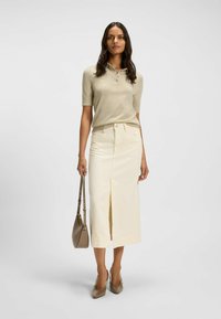 Beige kortärmad polo-shirty, krämfärgad midikjol med framfall, kombinerad med ljusbruna klackar och en matchande axelväska.