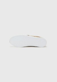 Sneaker featuring a brown upper, white rubber sole with textured grip pattern, and a minimalist design. No visible logos or embellishments.